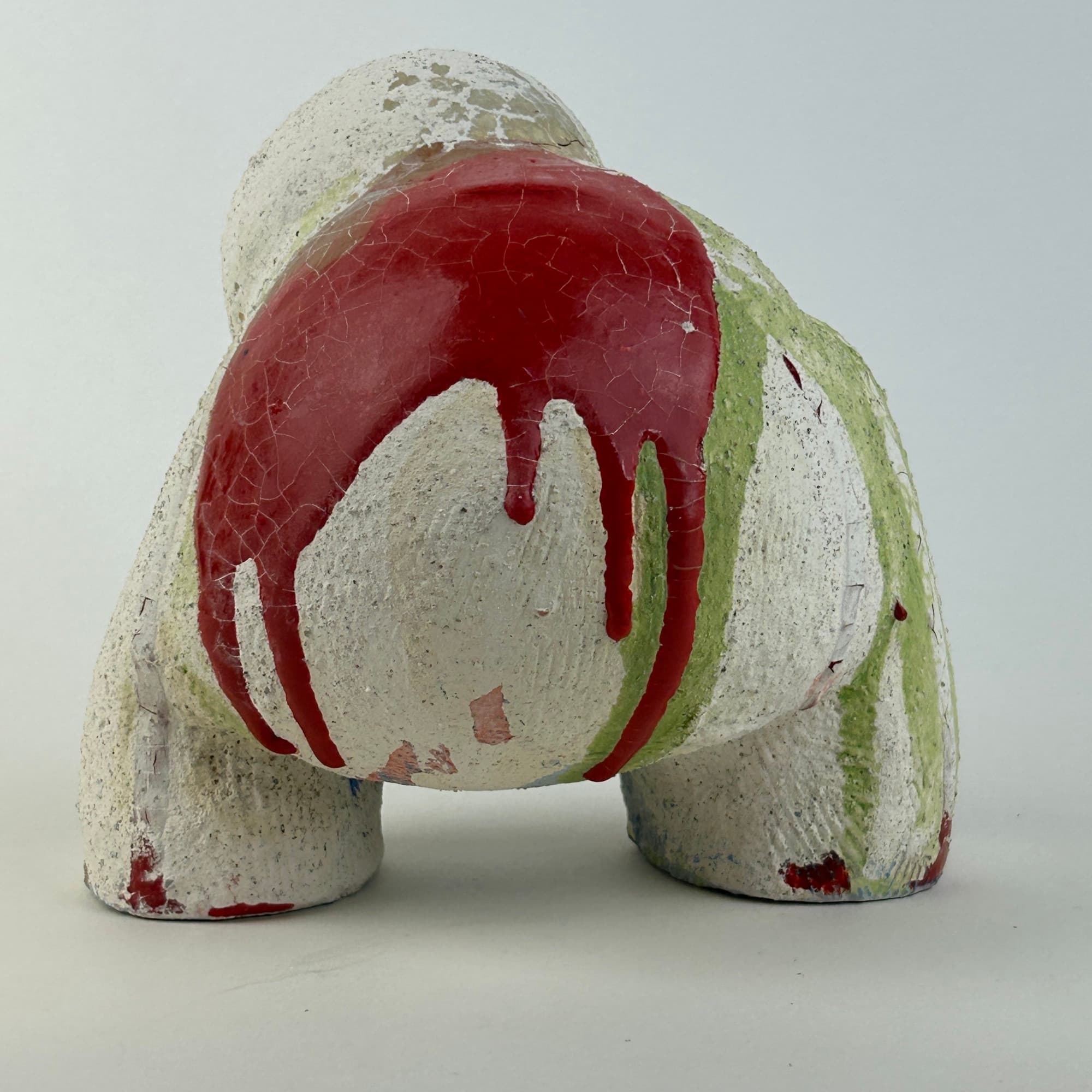 Chalk-white ceramic sculpture on four stub legs, with red and green glaze poured over the shoulder and pooling in the crevices.