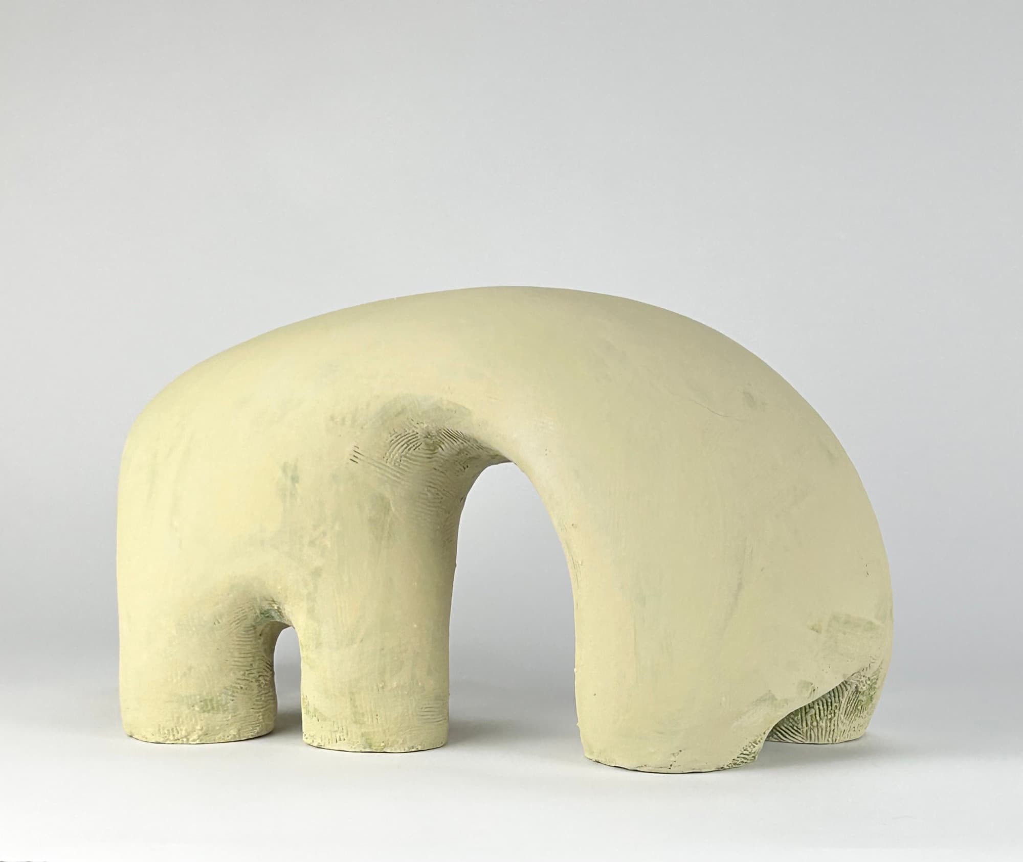 Pale cream ceramic arch resting on four tapered legs, the unglazed surface scraped and combed.