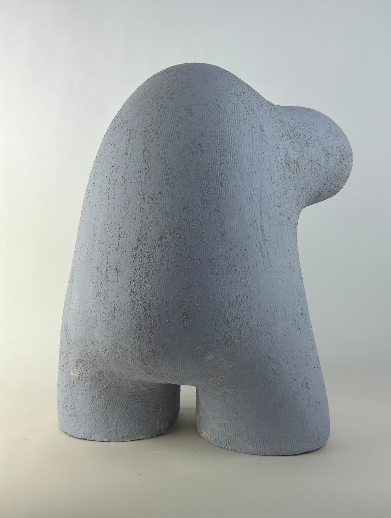 Upright ceramic sculpture in matte grey-blue, a small rounded knob at the crest above a broad speckled body.