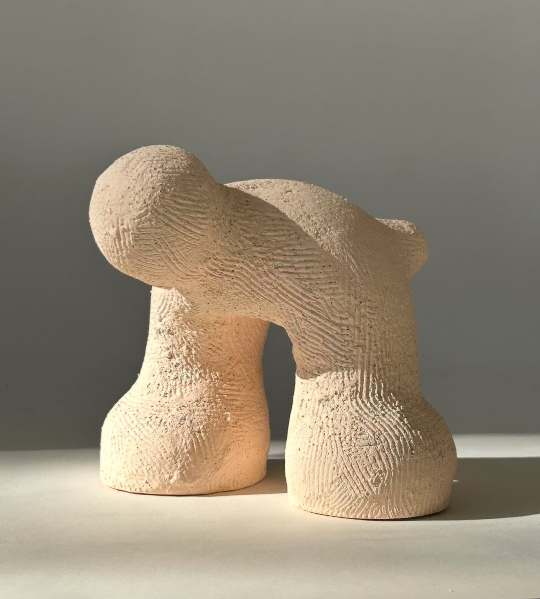 Unglazed blush-toned ceramic arch in raking side light, the surface covered in fine combed marks.
