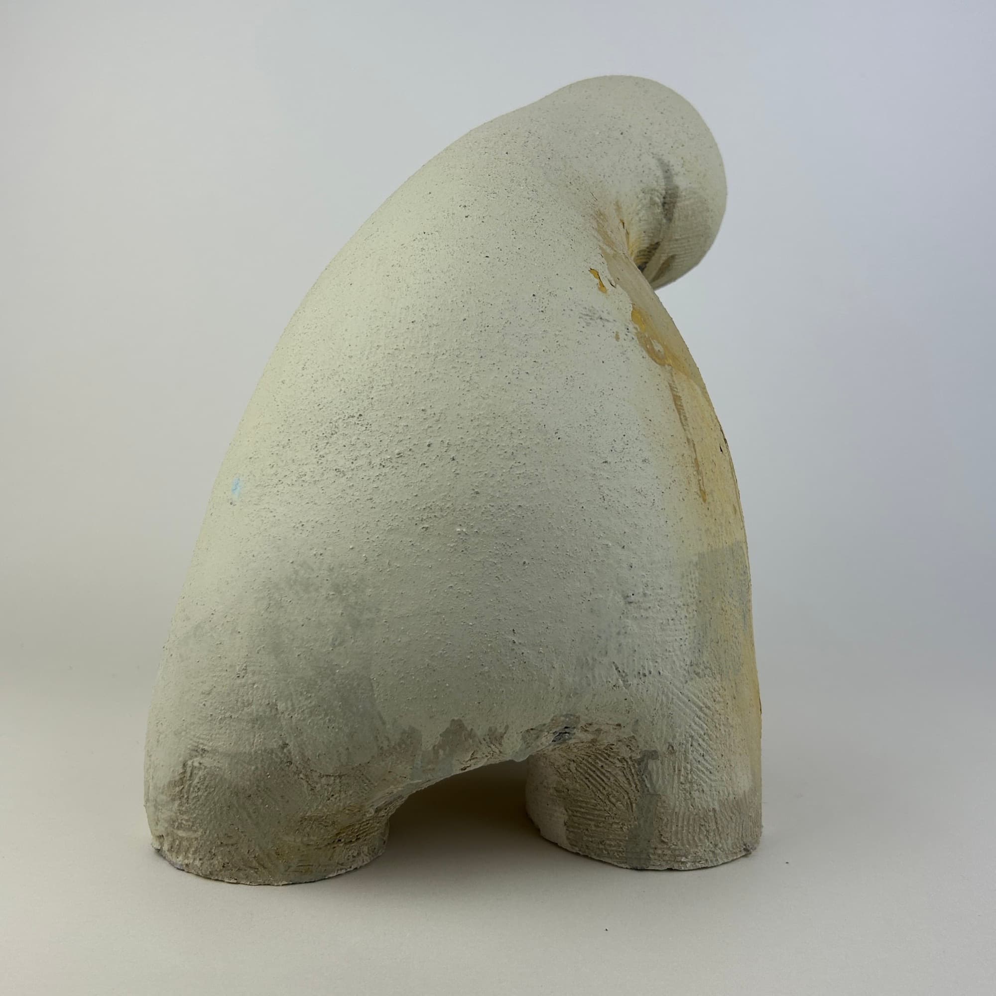 Off-white ceramic sculpture curving forward like a hood, standing on two short legs.