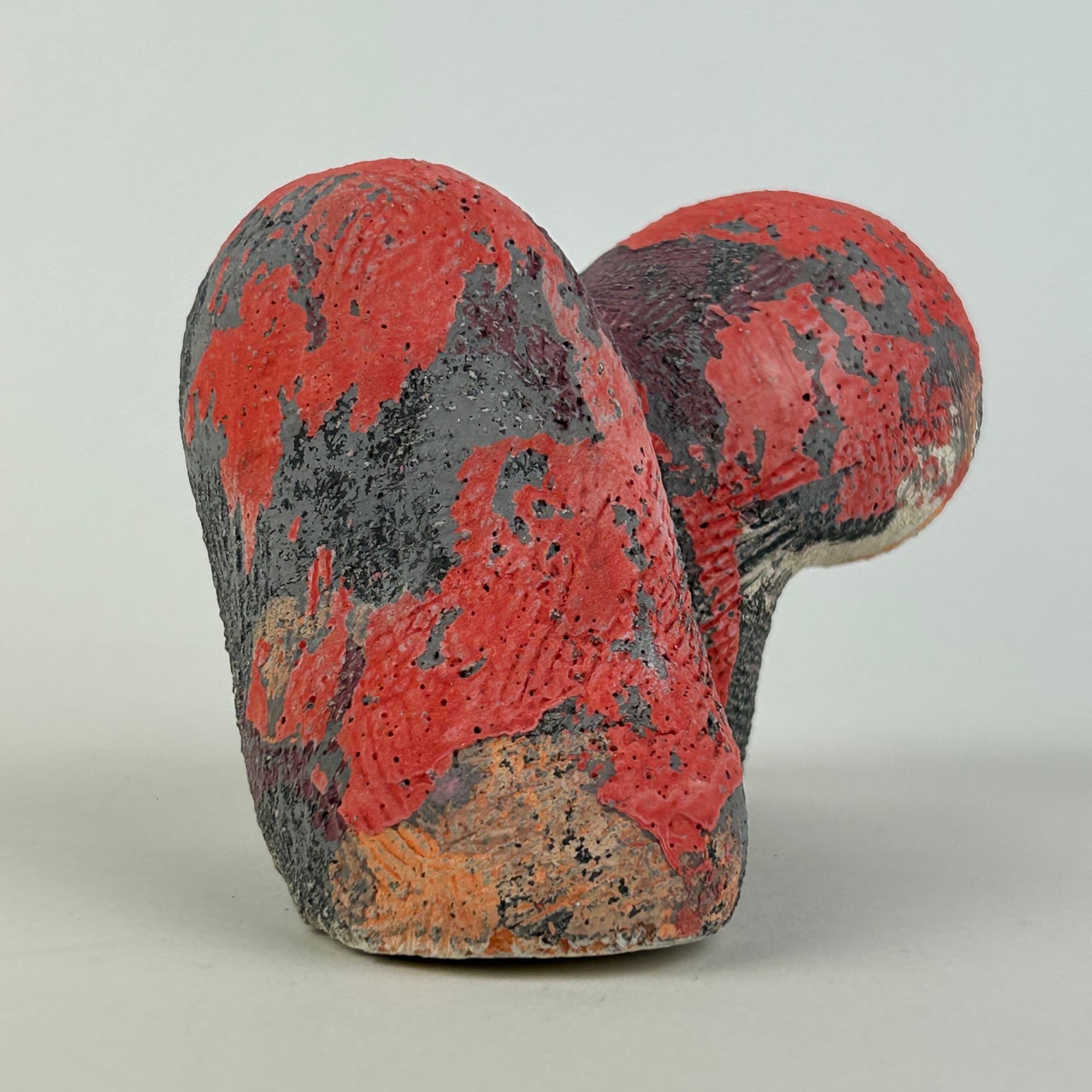 Compact ceramic sculpture mottled in red, charcoal and grey, its two lobes leaning together.