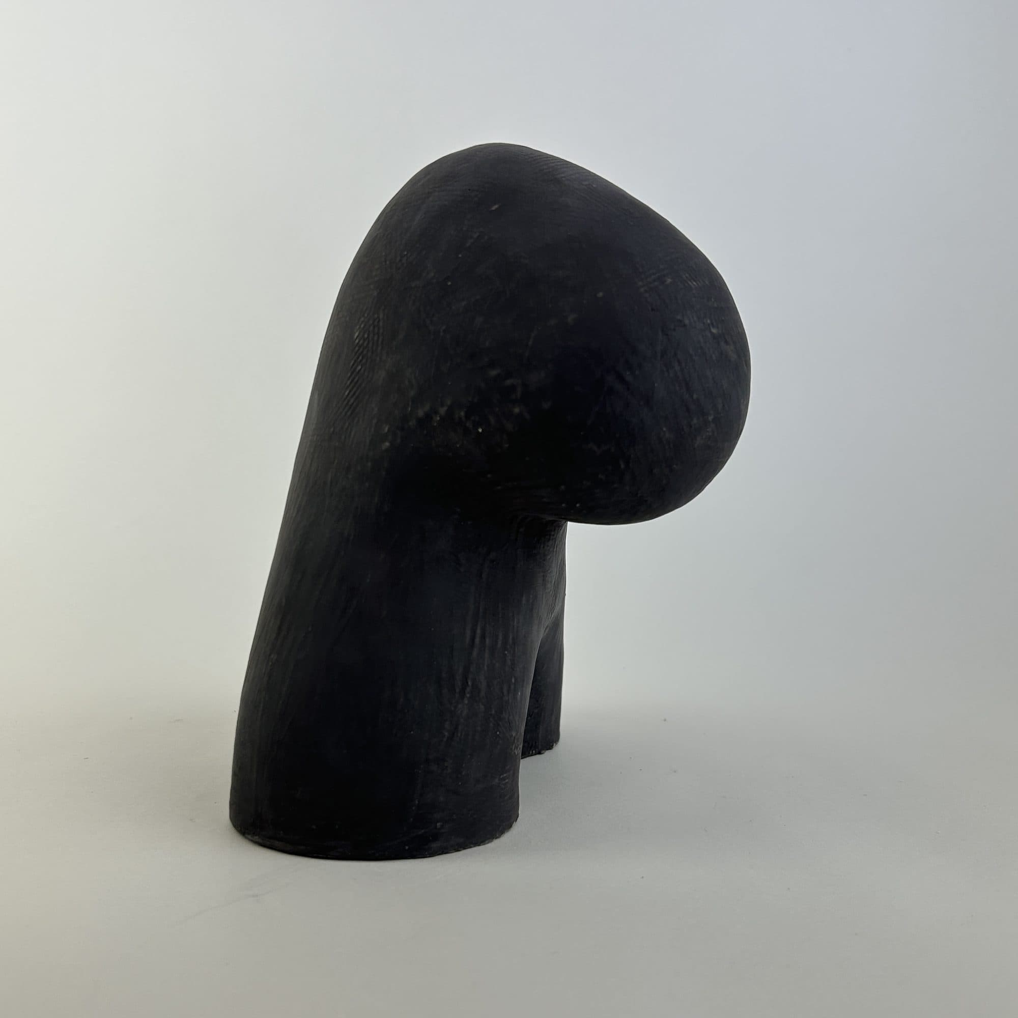Charcoal-black ceramic sculpture, the rounded head folded forward over a solid standing body.