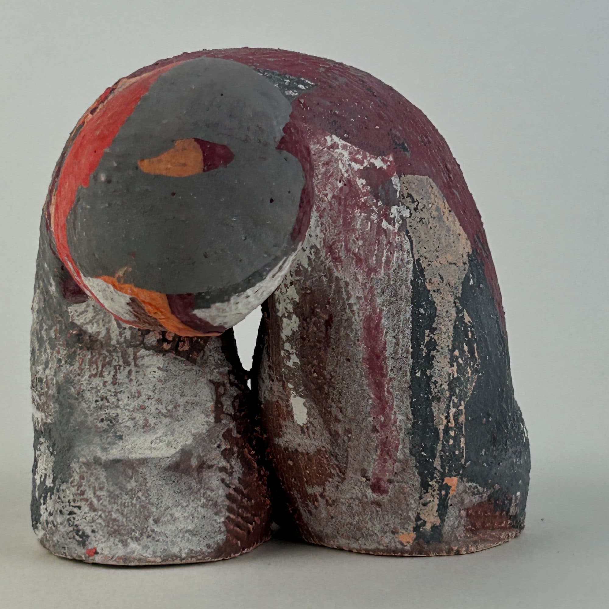 Ceramic sculpture mottled in red, grey and plum, a heavy rounded head leaning against the body.