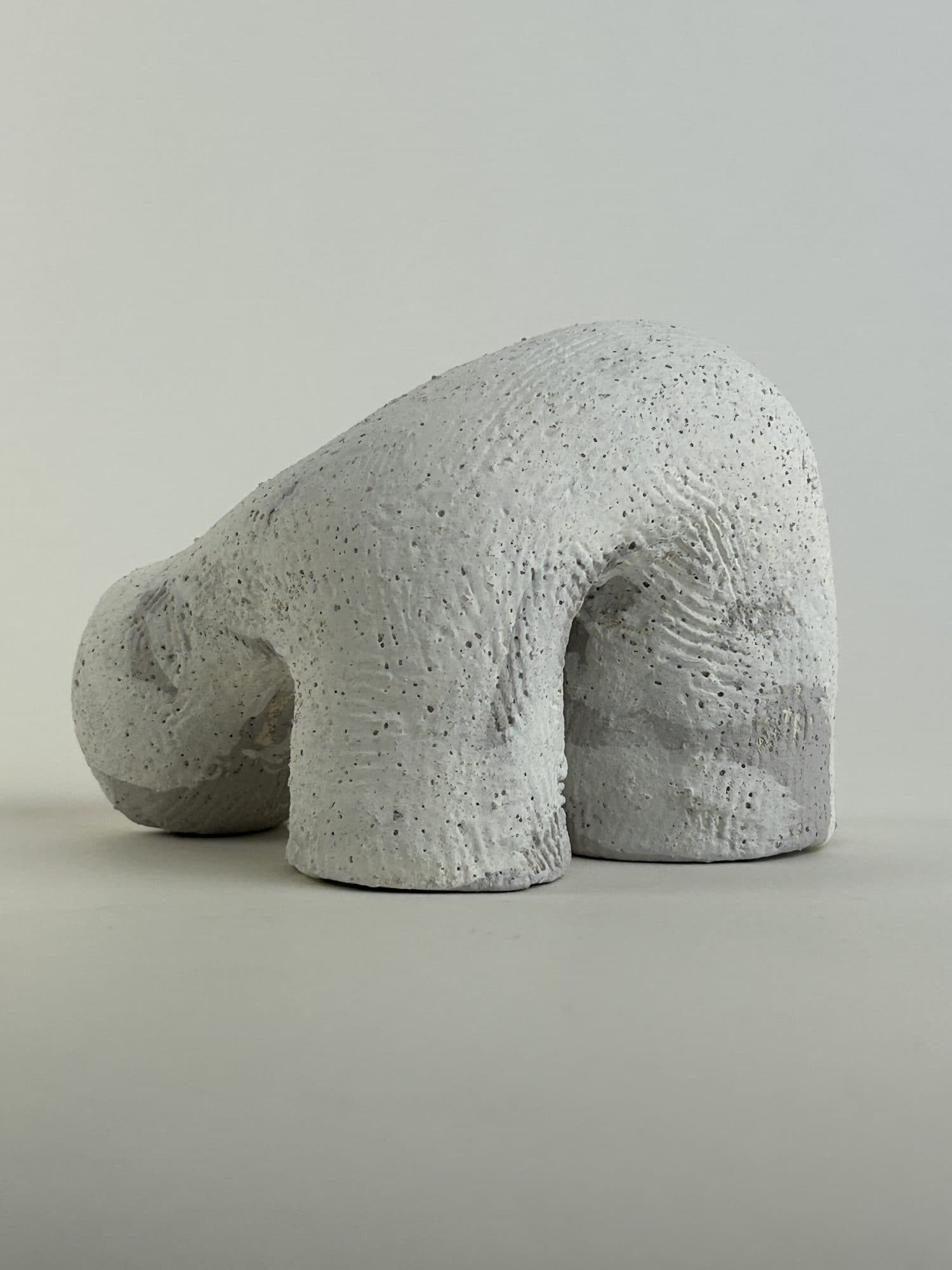 Small chalk-white ceramic sculpture crouching low, the surface left unglazed and combed.