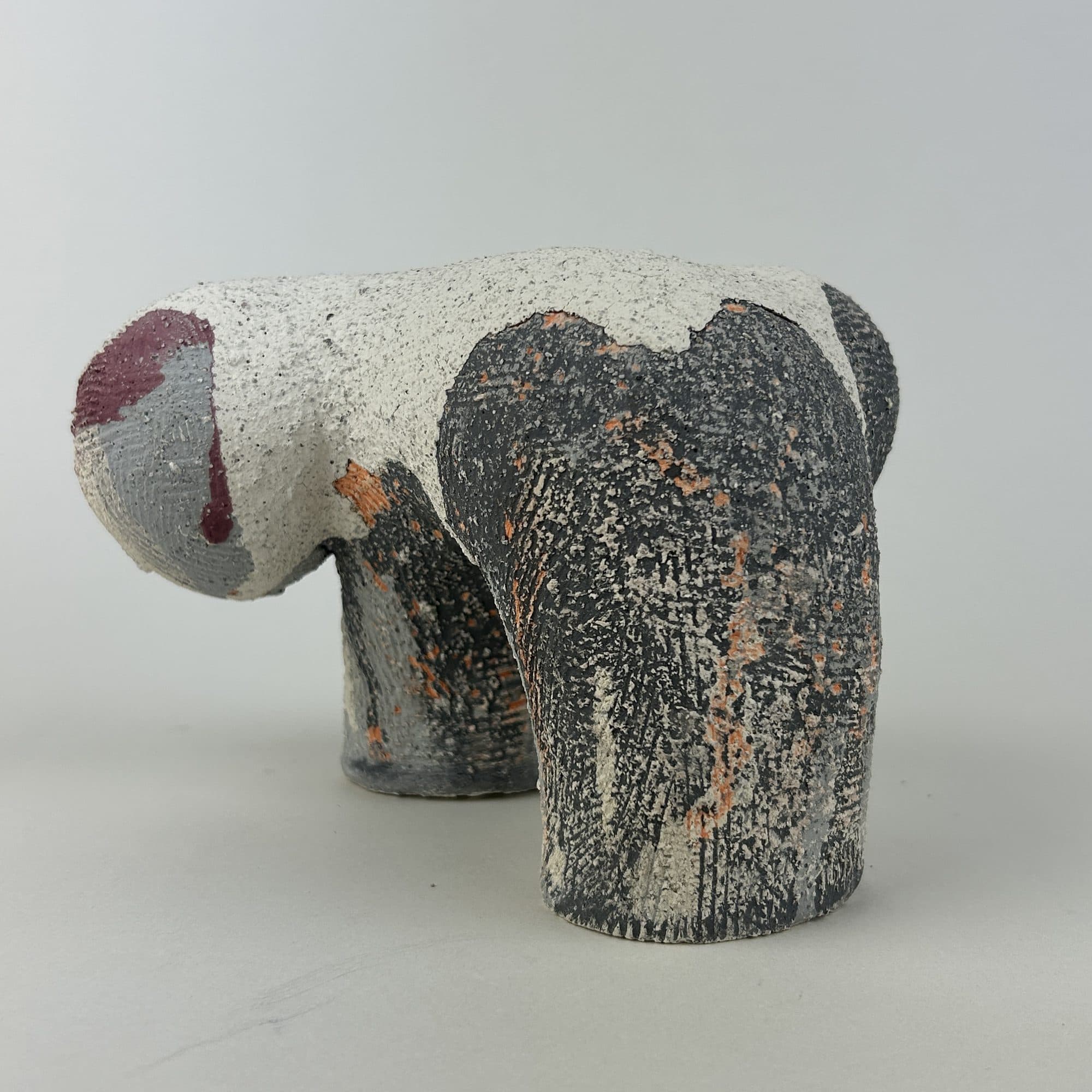 Ceramic sculpture in white and charcoal, standing on short stub legs.