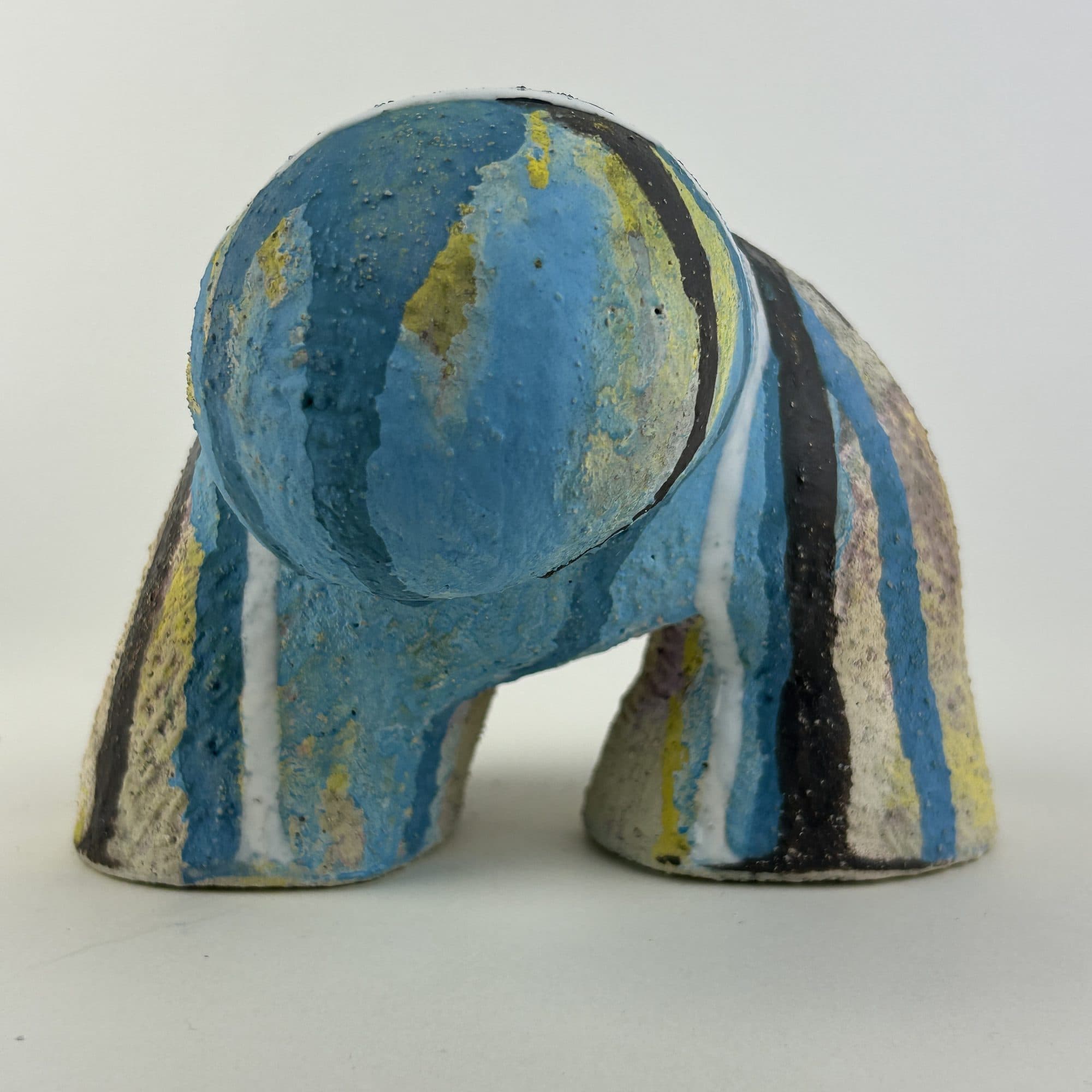 Four-legged ceramic sculpture striped in blue, yellow and black over a pale ground.