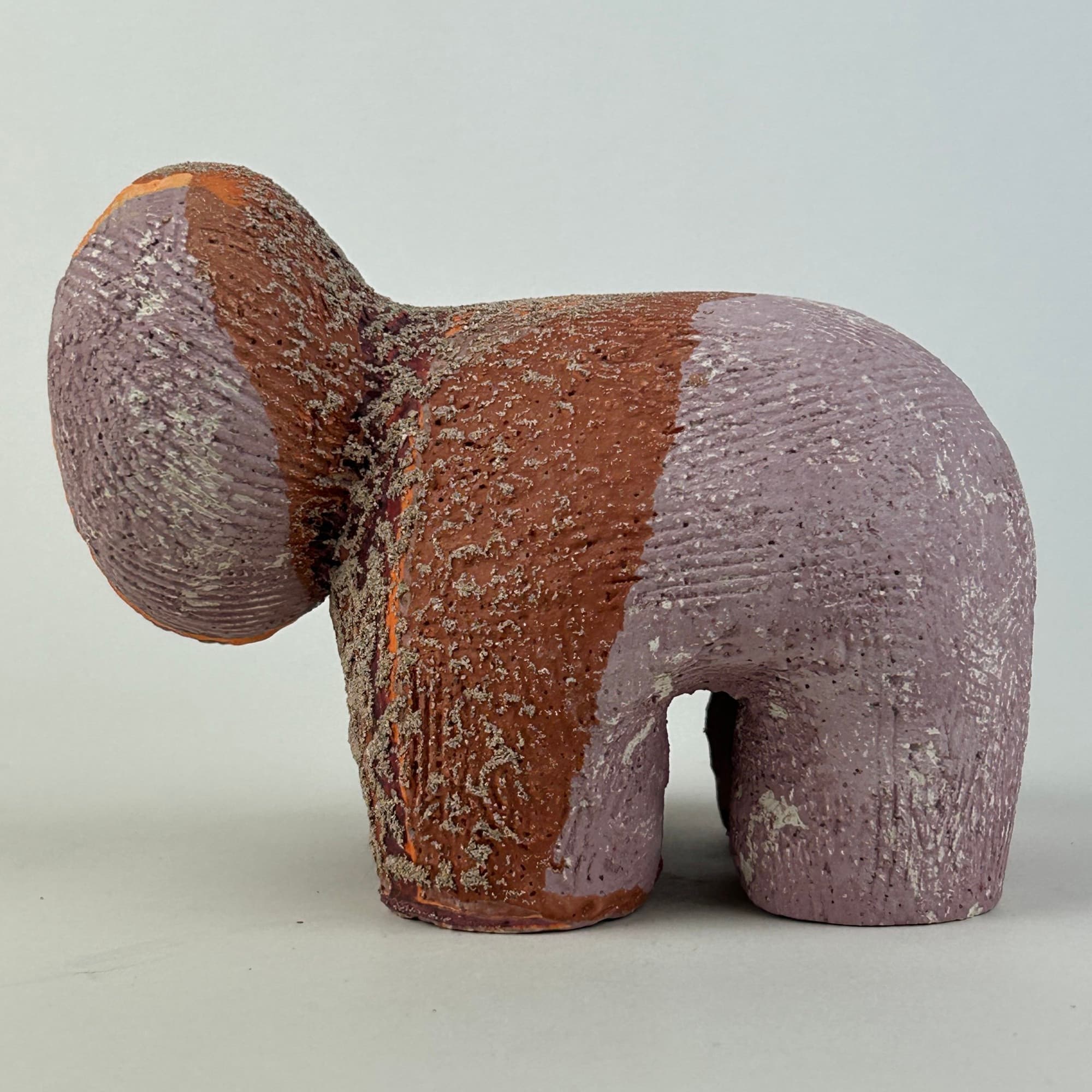 Four-legged ceramic sculpture in mauve and raw terracotta, heavily combed and speckled, with a rounded bulb at one end.