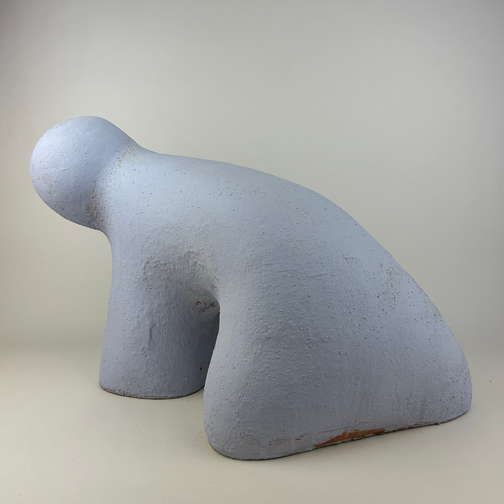 Crouching ceramic sculpture in powder blue, its long low back sweeping down to the ground and a rounded head turned aside.