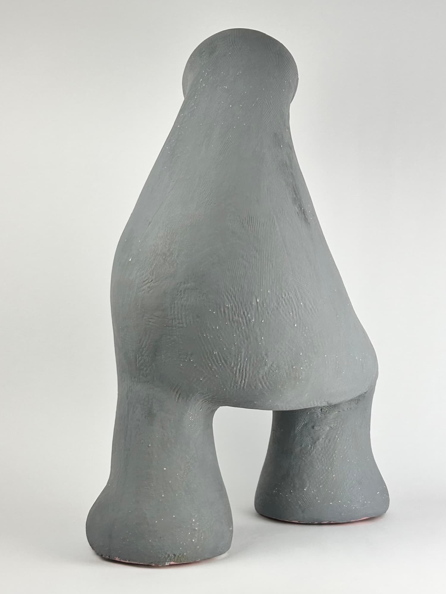 Matte grey ceramic sculpture on two tapered legs, the body rising to a smooth rounded point.