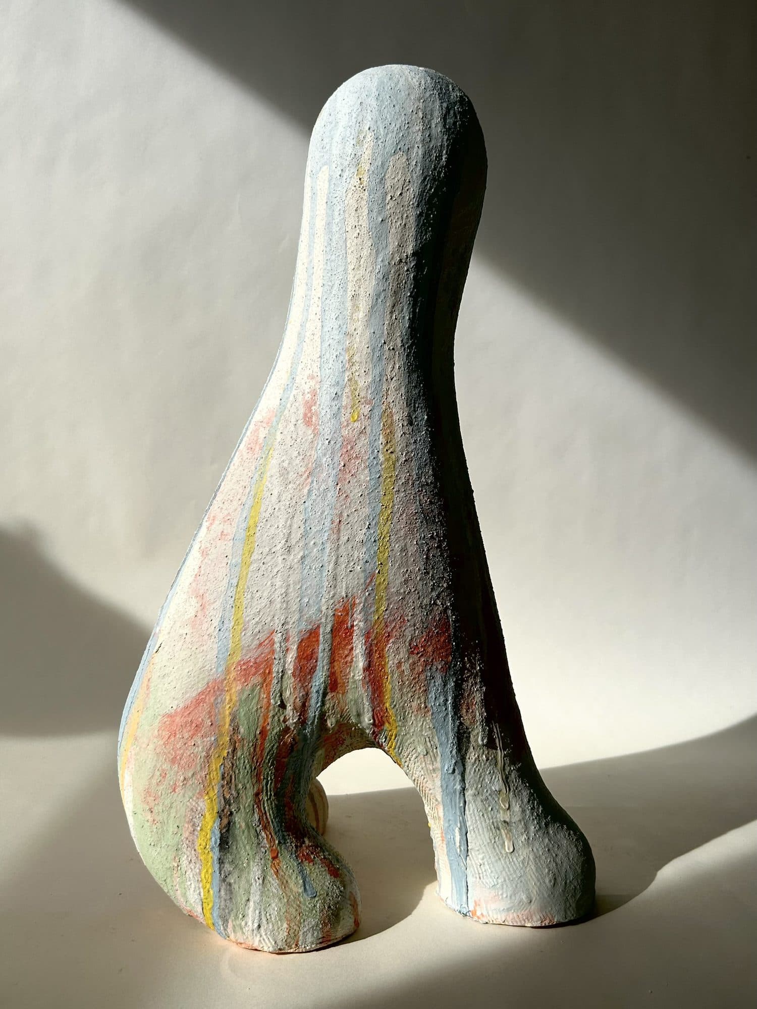 Tall ceramic sculpture streaked in pale blue and coral, with an opening cut through the base.