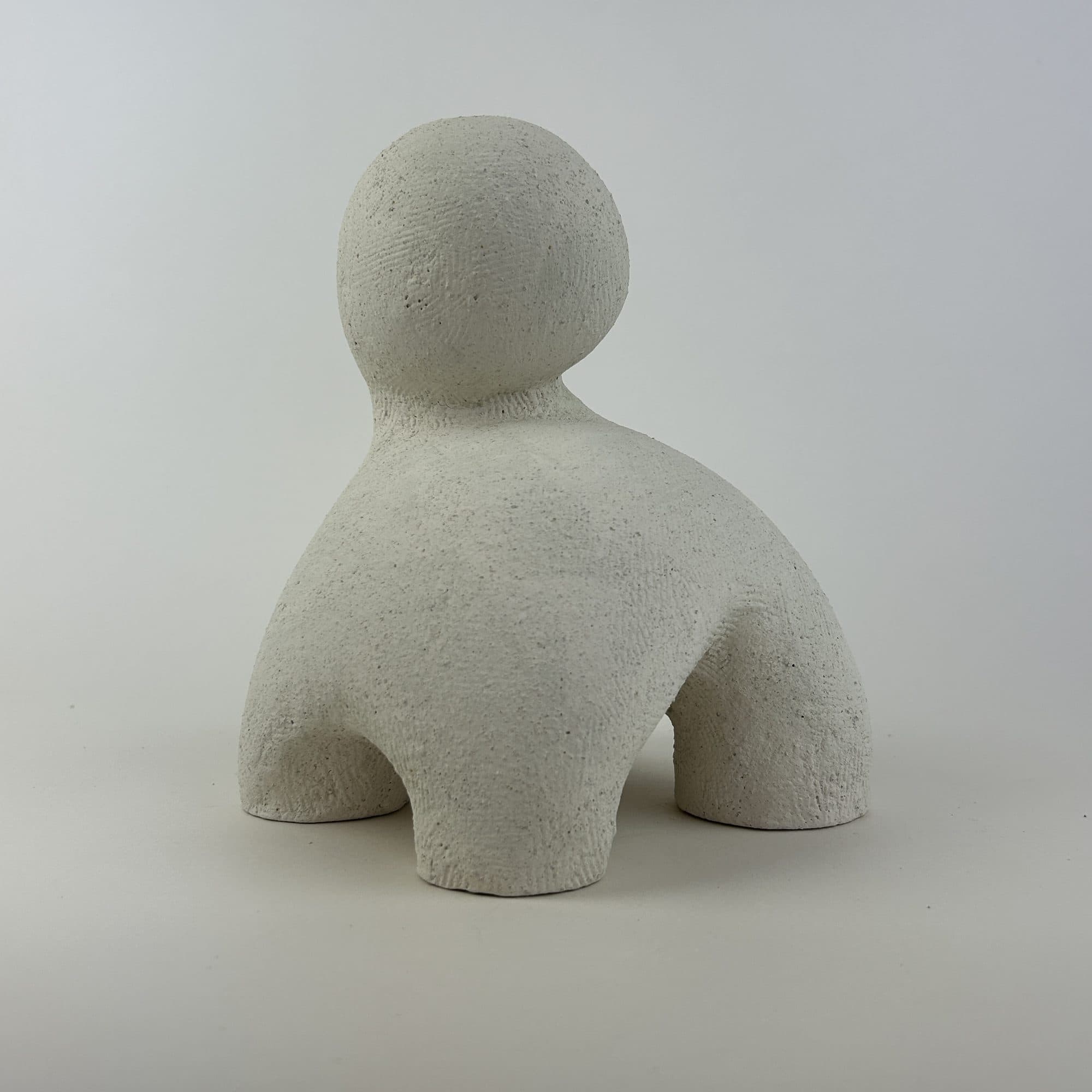 Small cream ceramic sculpture, a round head sitting on a heavy squared body.