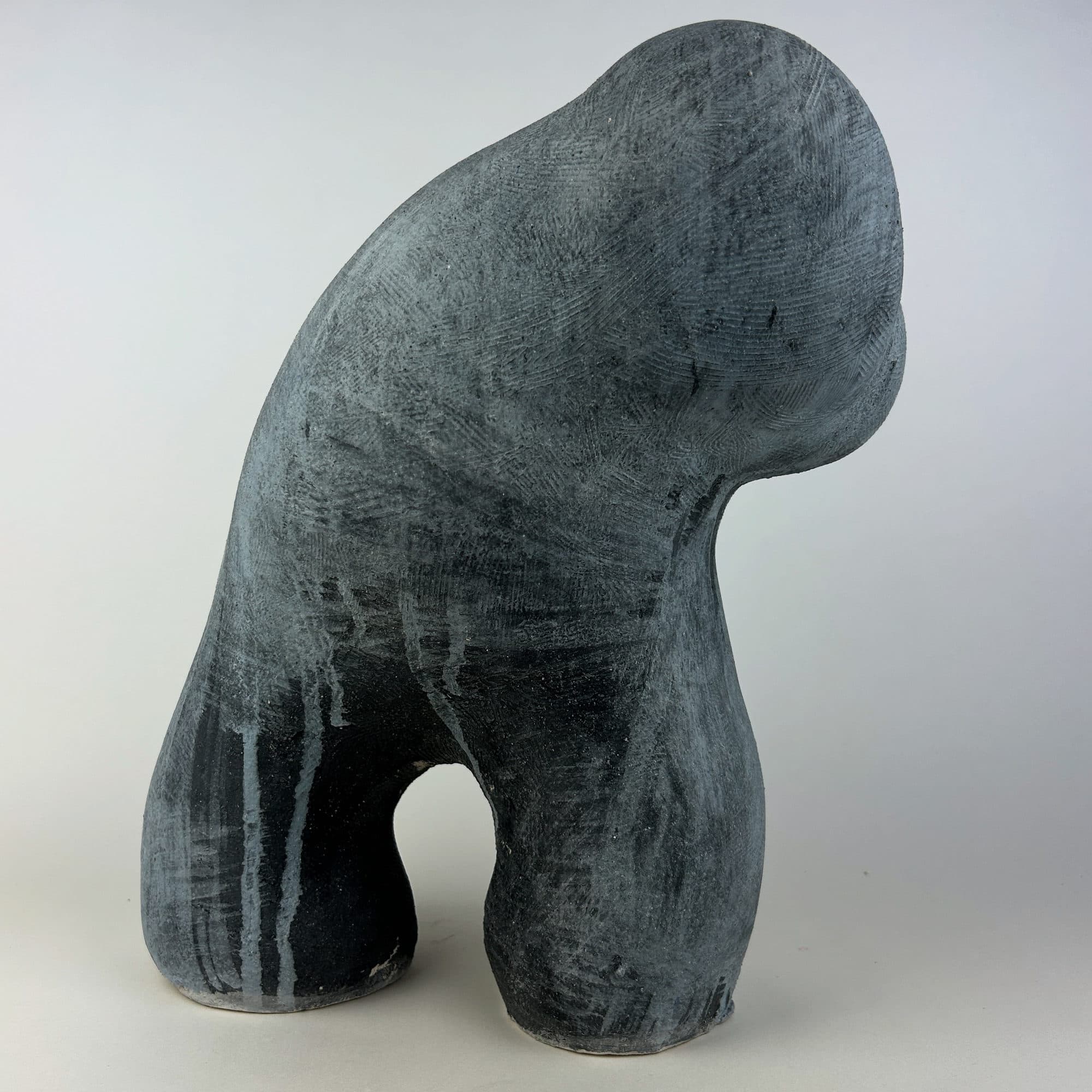 Ceramic sculpture in grey and black, a rounded head folded down over the shoulder.