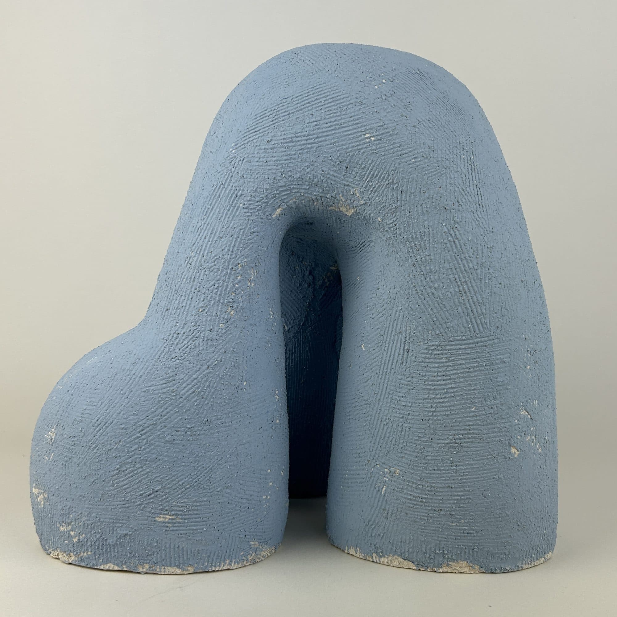 Powder-blue ceramic arch standing on two heavy legs, the surface densely combed.