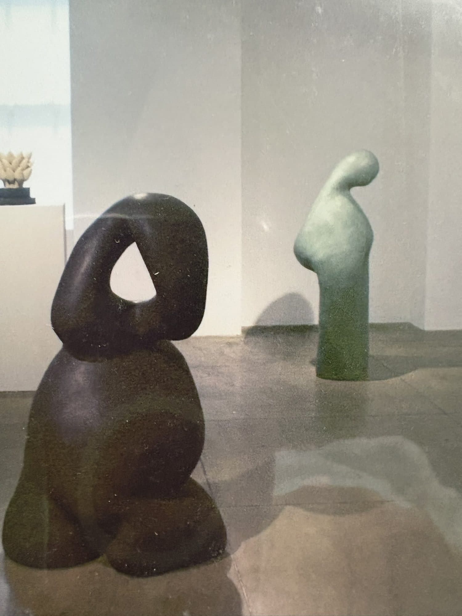 Two of Ashley D. James's ceramic sculptures installed on plinths in a gallery, one dark brown and one pale green.