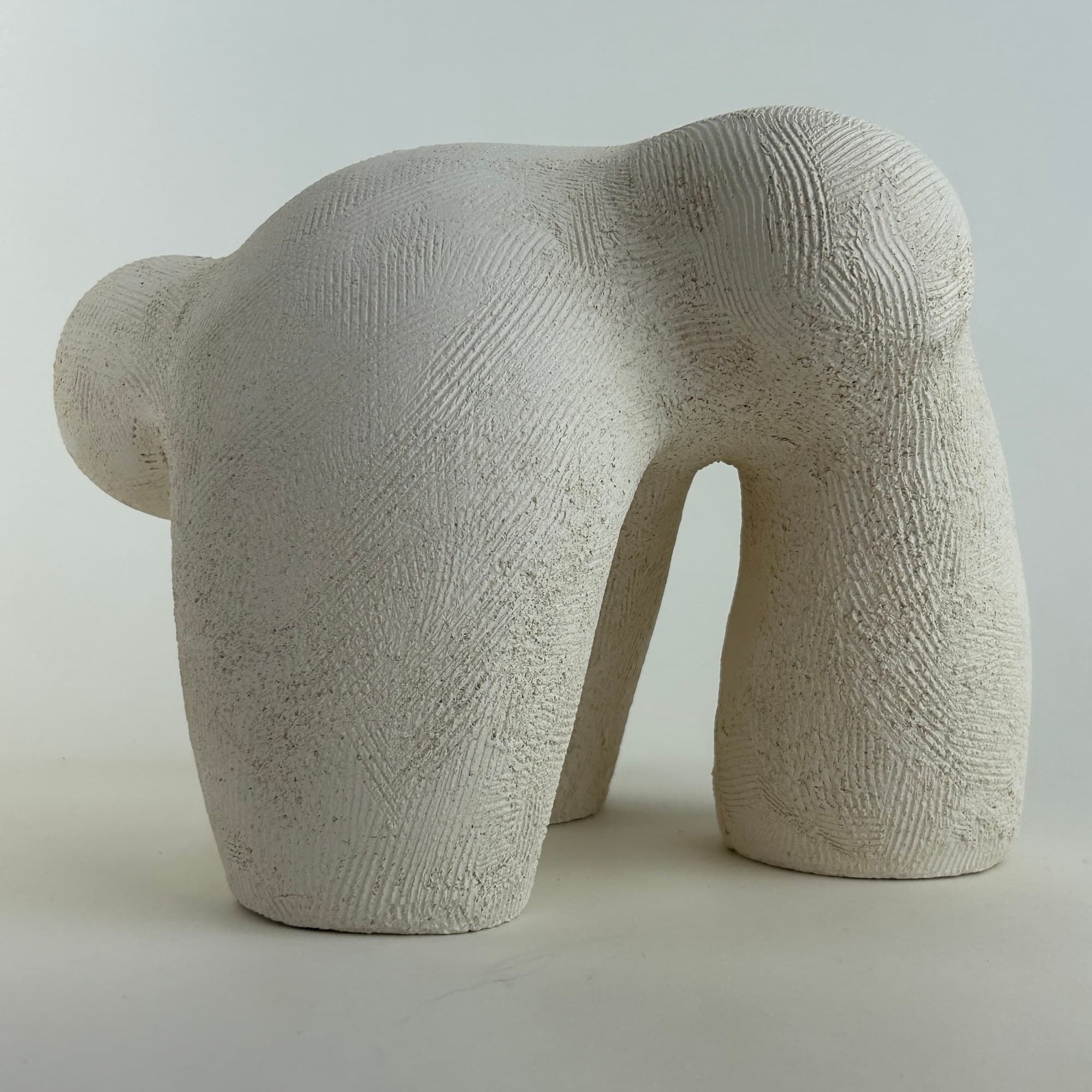 Hand-built ceramic sculpture in unglazed chalk-white clay, standing on four legs with a deeply combed surface.